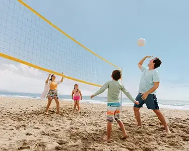 Volleyball family hero image Family of 4 playing volleyball at the beach