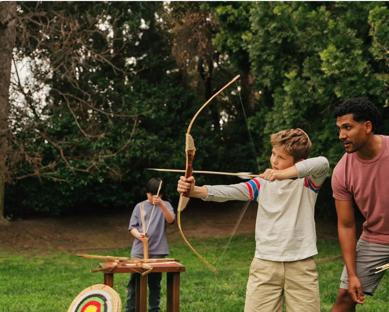Peds archery hero image Child using a bow and arrow with an adult supervising